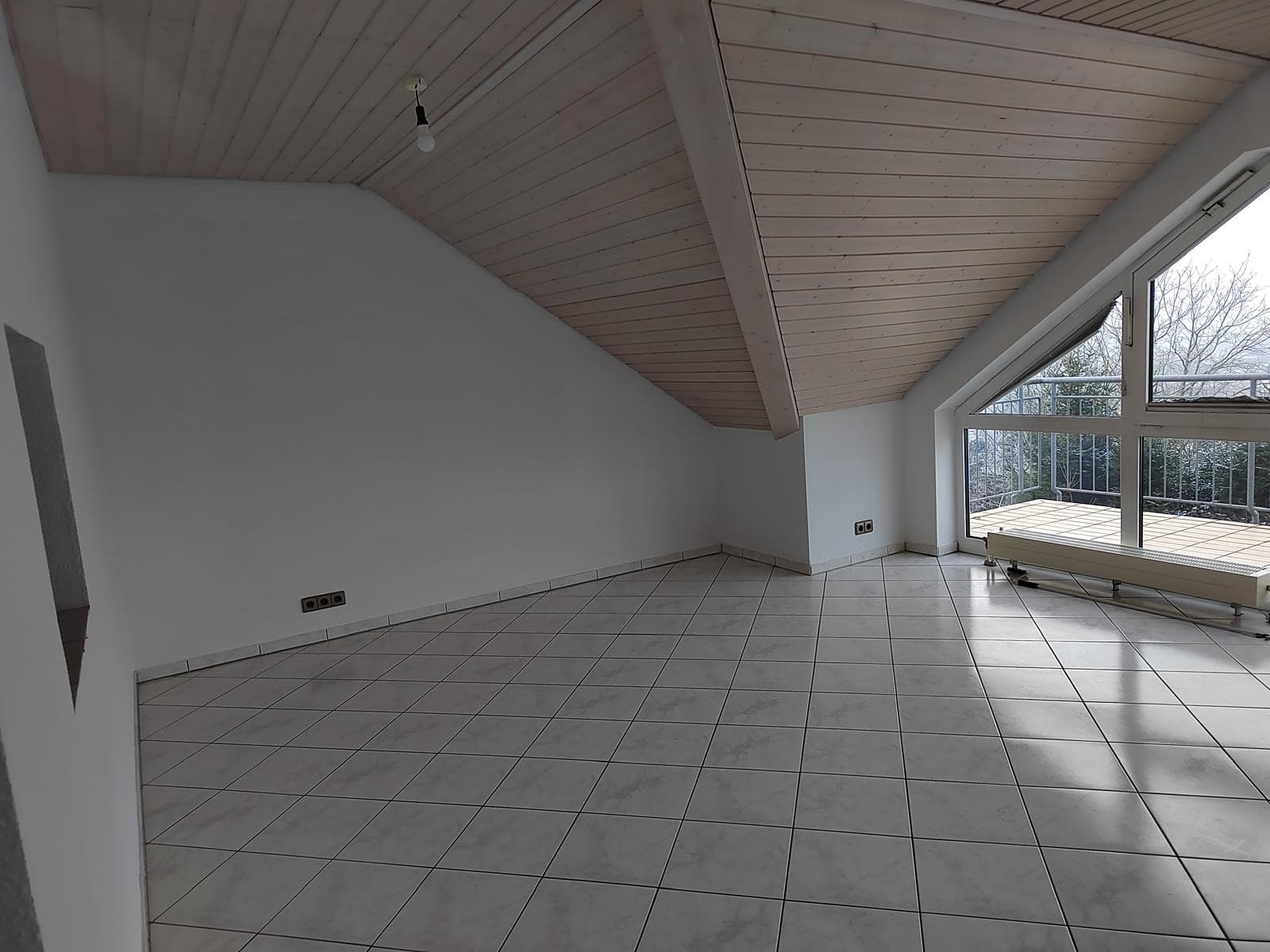 Leerer Wohnbereich mit Holzbalkendecke, grauen Fliesen und Tür zum Balkon